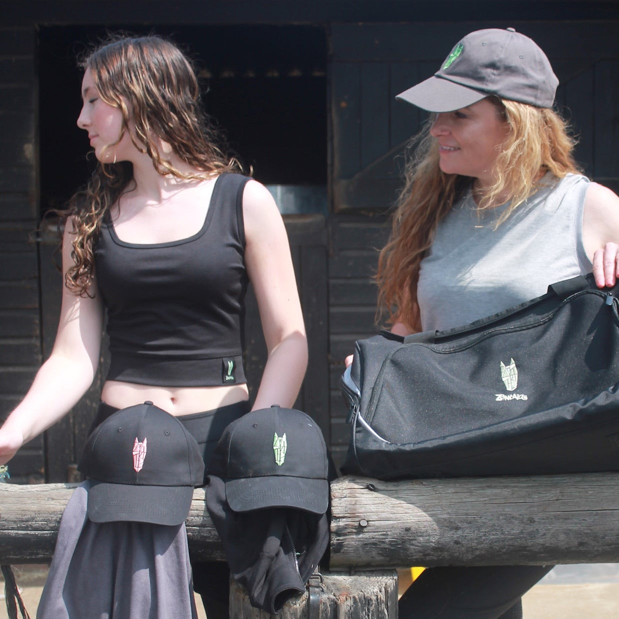 Two women wearing equestrian clothing and one of them wearing a black crop top with a silver green horse head logo