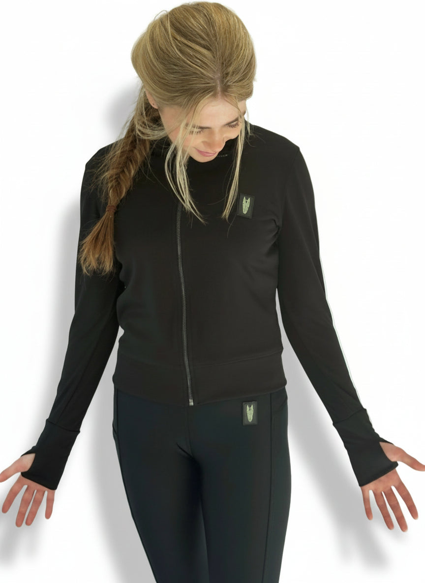 Young woman wearing a light equestrian jacket/cover up top with thumbholes, in black with a striking horse head logo on the left chest