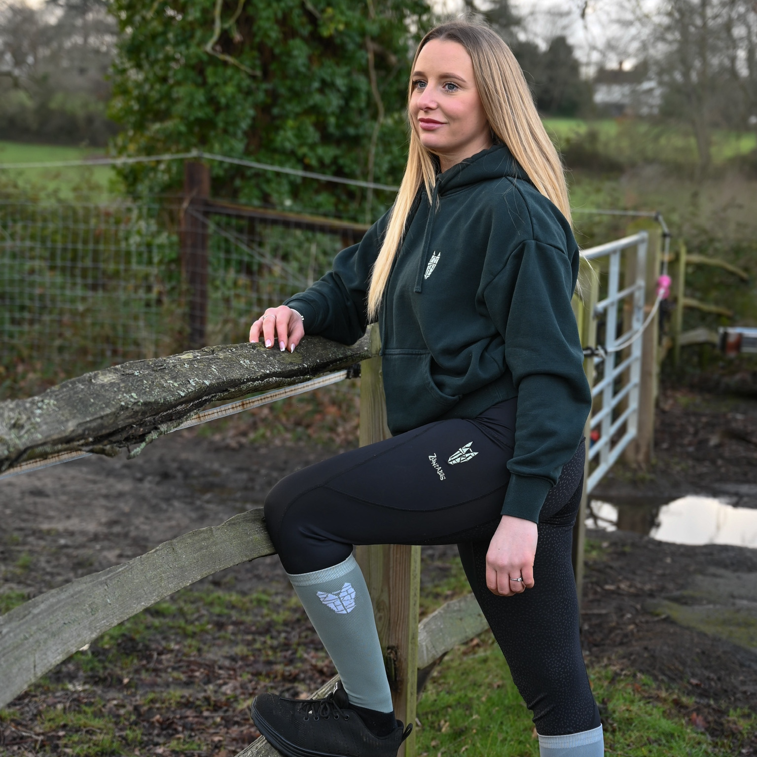 Woman in outdoor setting wearing a green hoodie and black leggings with light green equestrian socks.