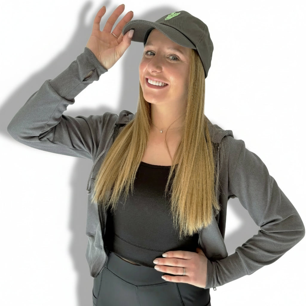 A woman wearing a gray Dad cap with a green logo on the front.