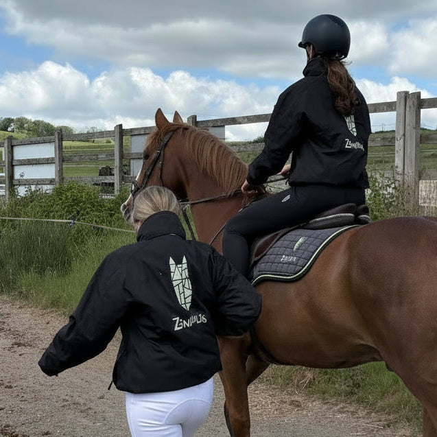 2 young women wearing black equestrian bomber jackets with a fashionable and striking logo featuring a geometric horse head icon