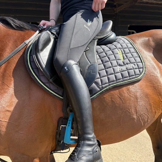 Woman sitting on a horse wearing black equestrian riding leggings a saddle and riding boots.