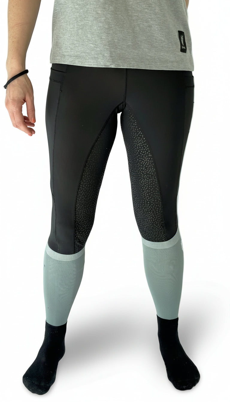 Woman facing forwards wearing black equestrian riding leggings with a full gel seat and double pockets