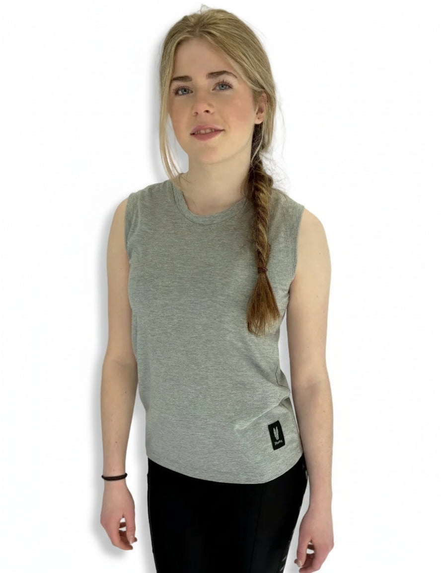 A teenage girl wearing a sleeveless gray t-shirt and black riding leggings, standing against a white background.