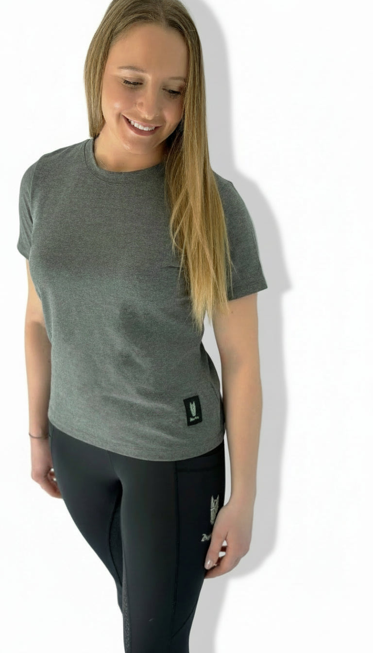 A woman wears a grey t-shirt with a striking grey green equestrian logo