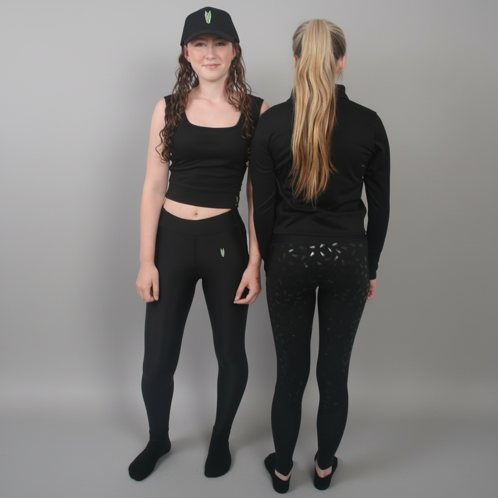 Two people wearing black riding leggings standing in front of a window with sunlight filtering through.