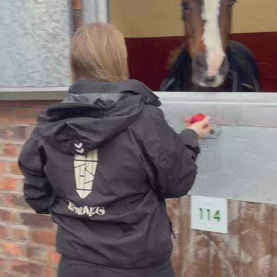 Woman wearing an equestrian bomber jacket feeding a horse an apple
