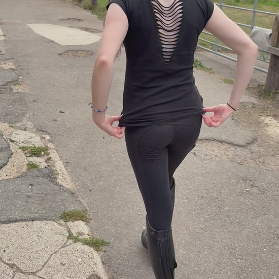 Video of young woman wearing equestrian black riding leggings and a trendy black tshirt with slashes across its back