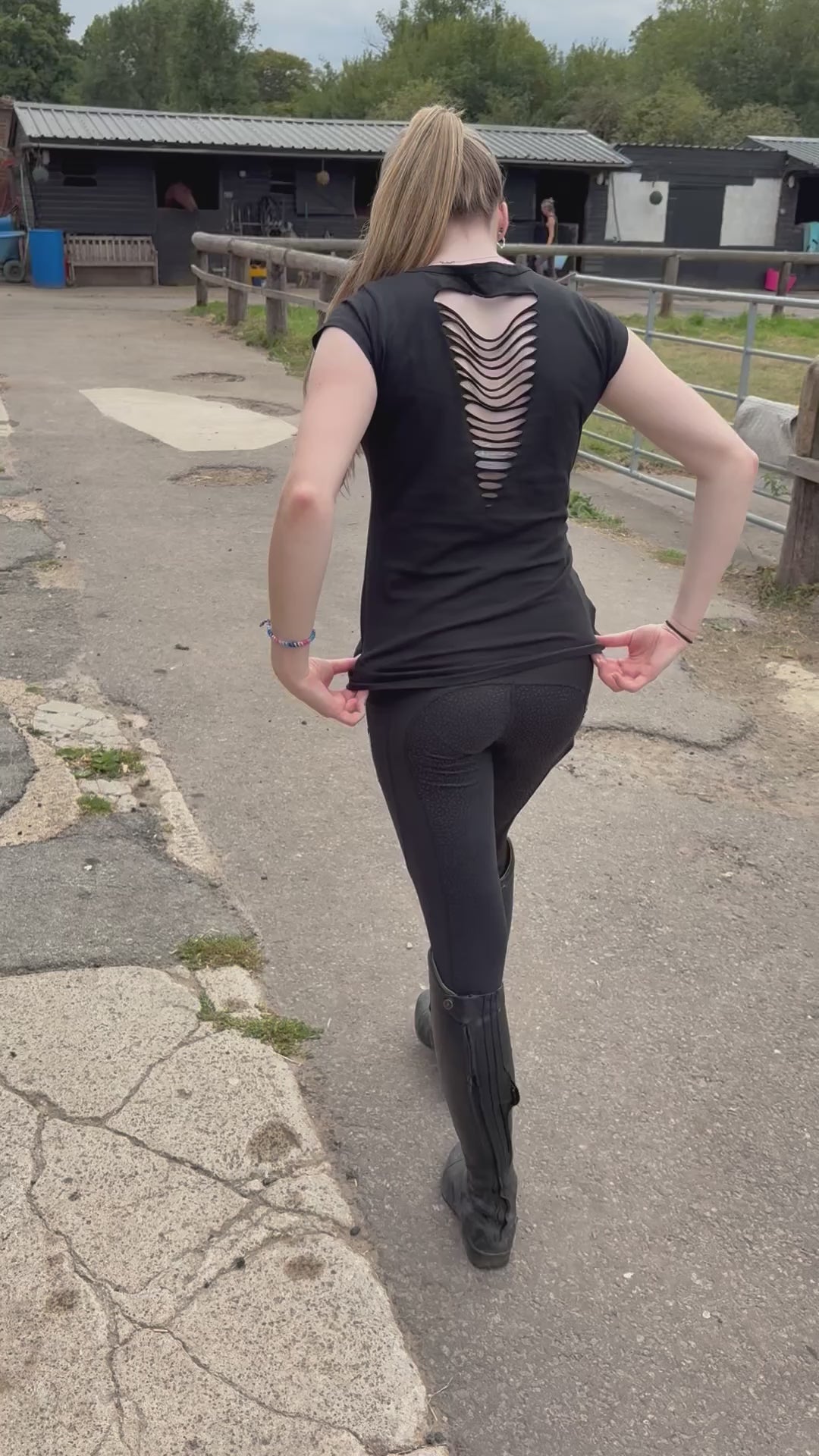 Video of young woman wearing equestrian black riding leggings and a trendy black tshirt with slashes across its back